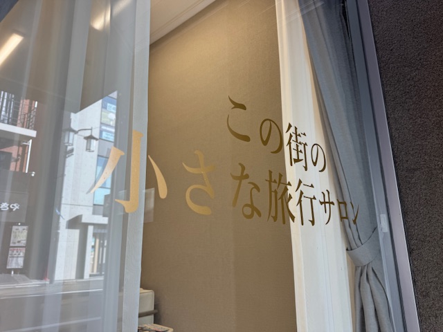 店頭窓ガラスに「この町の小さな旅行サロン」と案内