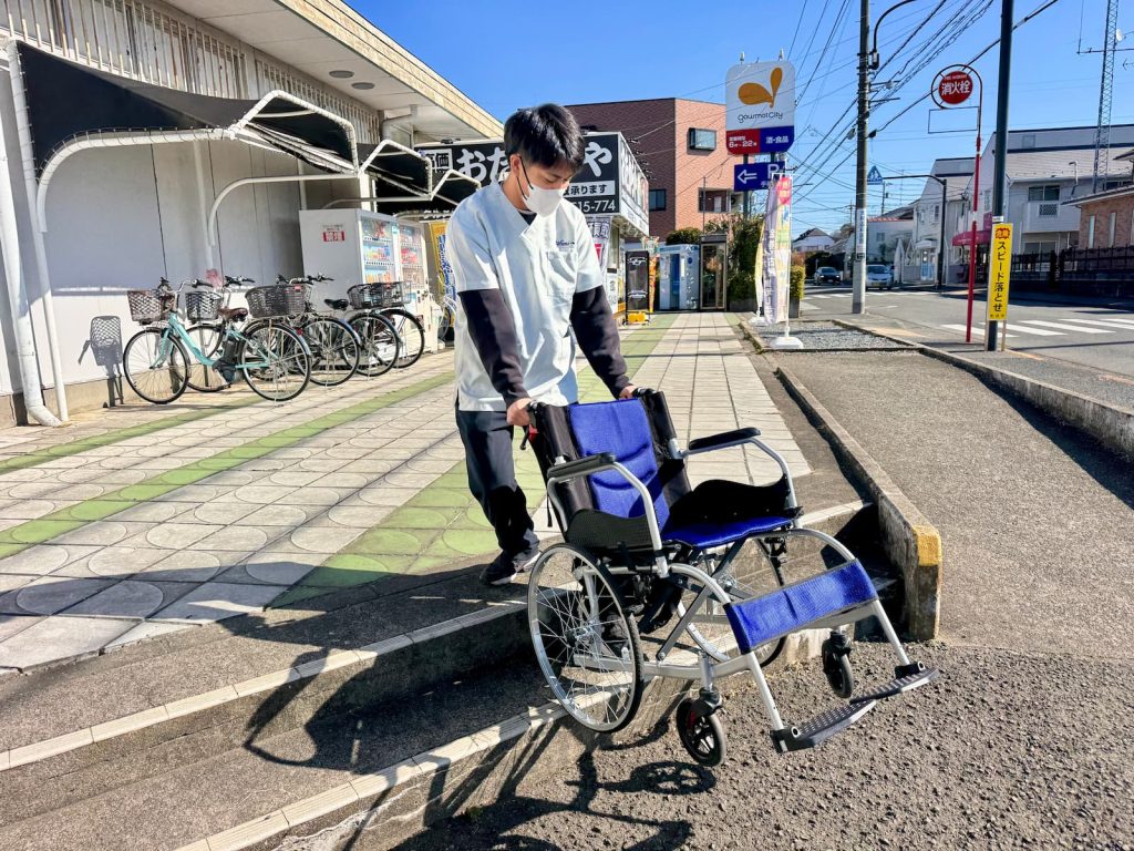 新人スタッフが車いすを使用し、スーパーの段差を活用して階段介助研修を行う様子｜町田の福祉介護タクシー Trip☆Care.