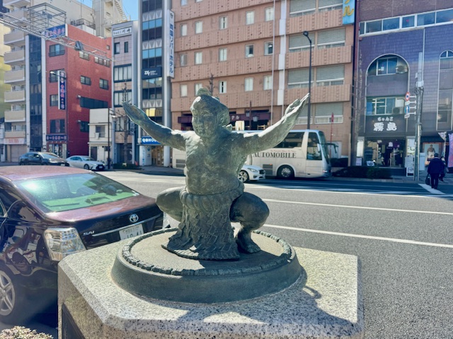 相撲取りの石像の後ろにちゃんこ霧島の食事施設
