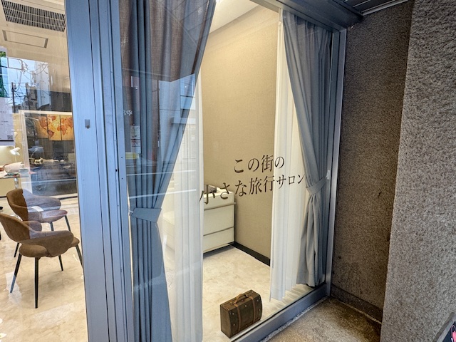 Trip☆Care.成城店の入口ガラスには「この街の小さな旅行サロン」の案内
